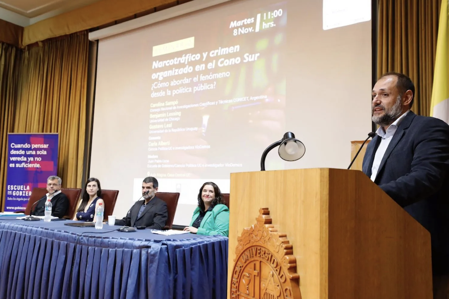 Persona a la derecha exponiendo en seminario y personas sentadas frente a una mesa al costado izquierdo del expositor.